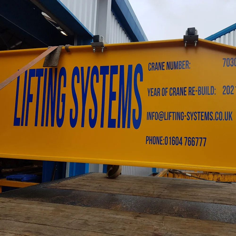 A wide shot of a high-bay industrial facility featuring a double-girder yellow overhead crane system mounted on blue steel runway beams, spanning the entire width of the building.